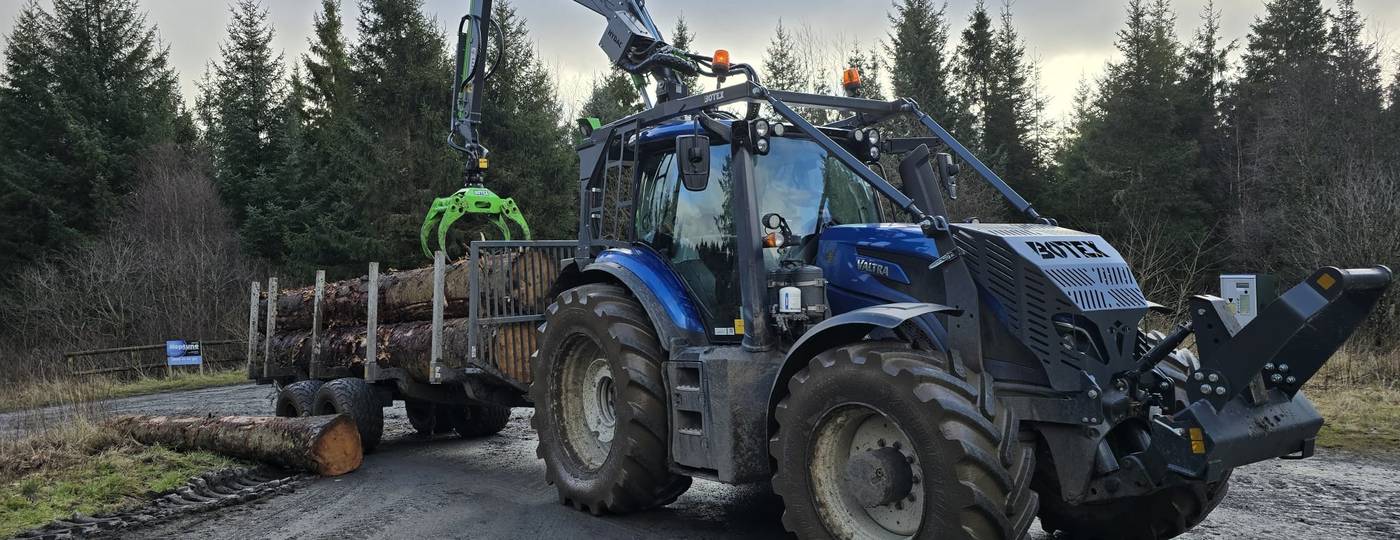 A tractor and timber trailer with loading crane at a forest roadside